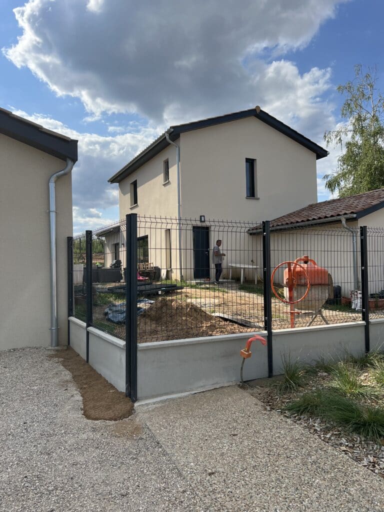 Clôture rigide sur muret béton pour maison moderne Maison moderne avec clôture rigide noire sur muret en béton, bétonnière et tas de terre dans le jardin en chantier.